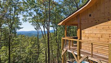 Una cabaña de madera con terraza y vistas a un bosque y montañas distantes.