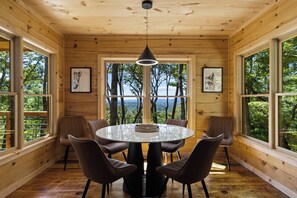 Un interior de madera con una mesa redonda y sillas, ventanas amplias y cuadros enmarcados.