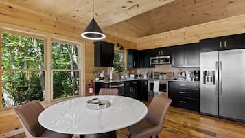 Une cuisine moderne avec une table à manger ronde, des meubles de rangement noirs, des appareils électroménagers en acier inoxydable et de grandes fenêtres.