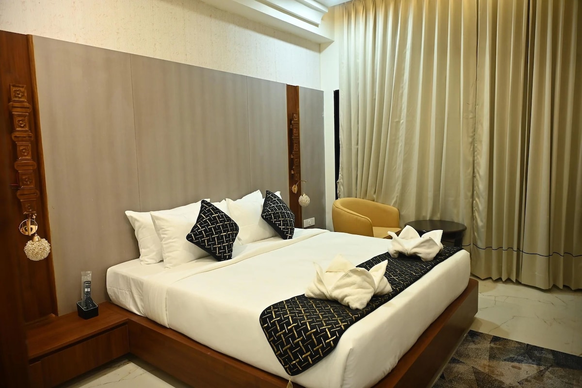 Ein Hotelzimmer mit einem großen Bett, einem hölzernen Kopfteil, einem Nachttisch mit Fernbedienung, einem gelben Sessel und einem Fenster mit Vorhängen.