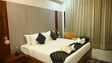 A hotel room with a large bed, a wooden headboard, a bedside table with a remote control, a yellow armchair, and a window with curtains.