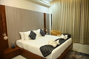 Ein Hotelzimmer mit einem großen Bett, einem hölzernen Kopfteil, einem Nachttisch mit Fernbedienung, einem gelben Sessel und einem Fenster mit Vorhängen.