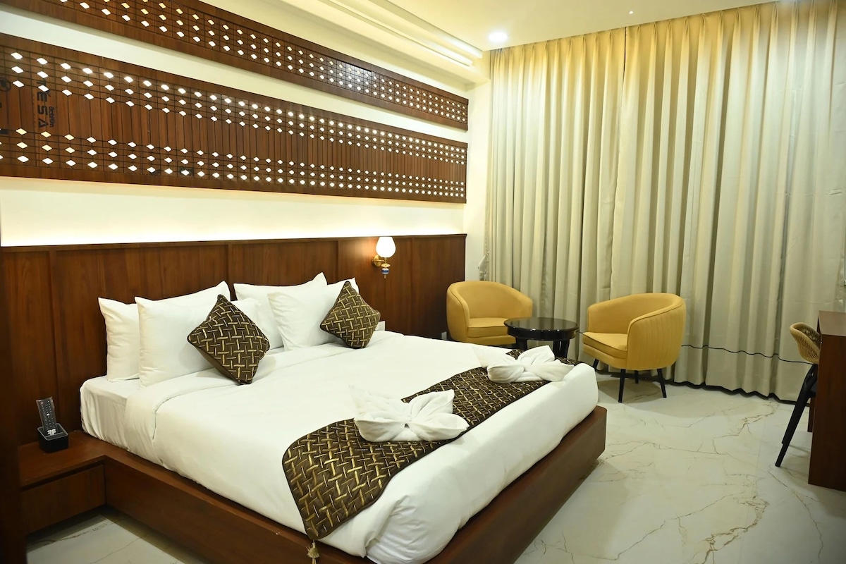 Ein Hotelzimmer mit einem großen Bett, zwei Stühlen, einem kleinen Tisch und einer dekorativen Holzverkleidung über dem Bett.