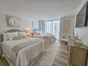 A bedroom with two beds, a bedside table with a lamp, a chair, and a view of the outside. - North Hampton 1406 | Luxury Remodel | Ocean Views | Sleeps 10 (Myrtle Beach)