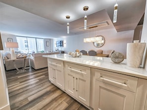 A modern kitchen with a marble countertop, wooden cabinets, and pendant lighting. - North Hampton 1406 | Luxury Remodel | Ocean Views | Sleeps 10 (Myrtle Beach)