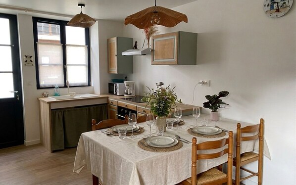 A dining area with a table set for four, a kitchen in the background, and a clock on the wall. - Holiday home near the beaches (Batz-sur-Mer)