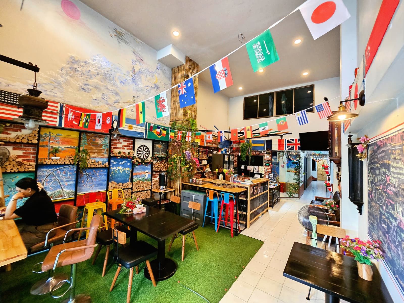 A restaurant with multiple tables and chairs, a variety of flags hanging from the ceiling, and a wall with framed artwork.