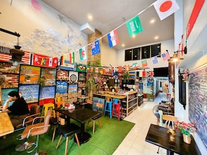 A restaurant with multiple tables and chairs, a variety of flags hanging from the ceiling, and a wall with framed artwork. - MT FRIEND HOME (Phuket)