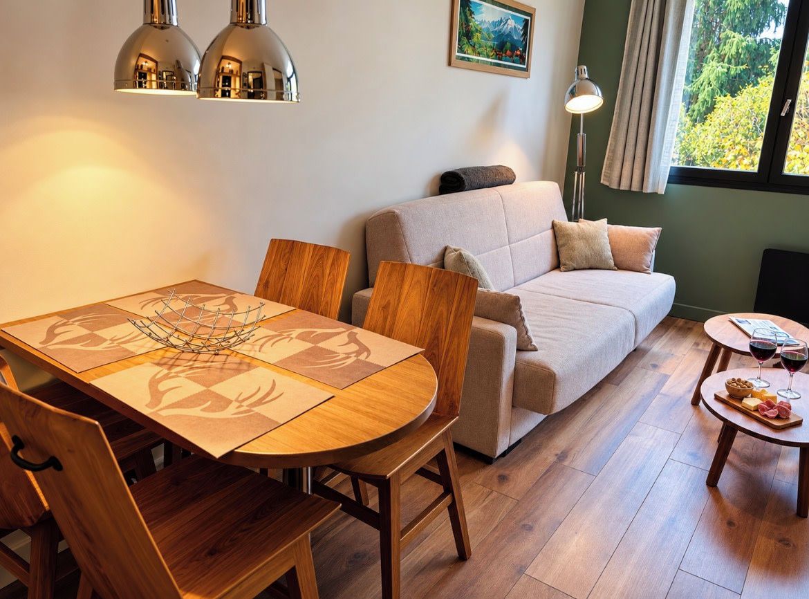 Una sala acogedora con sofá, una mesa de comedor con sillas y una mesita auxiliar con vasos y aperitivos.