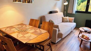 Una sala acogedora con sofá, una mesa de comedor con sillas y una mesita auxiliar con vasos y aperitivos.