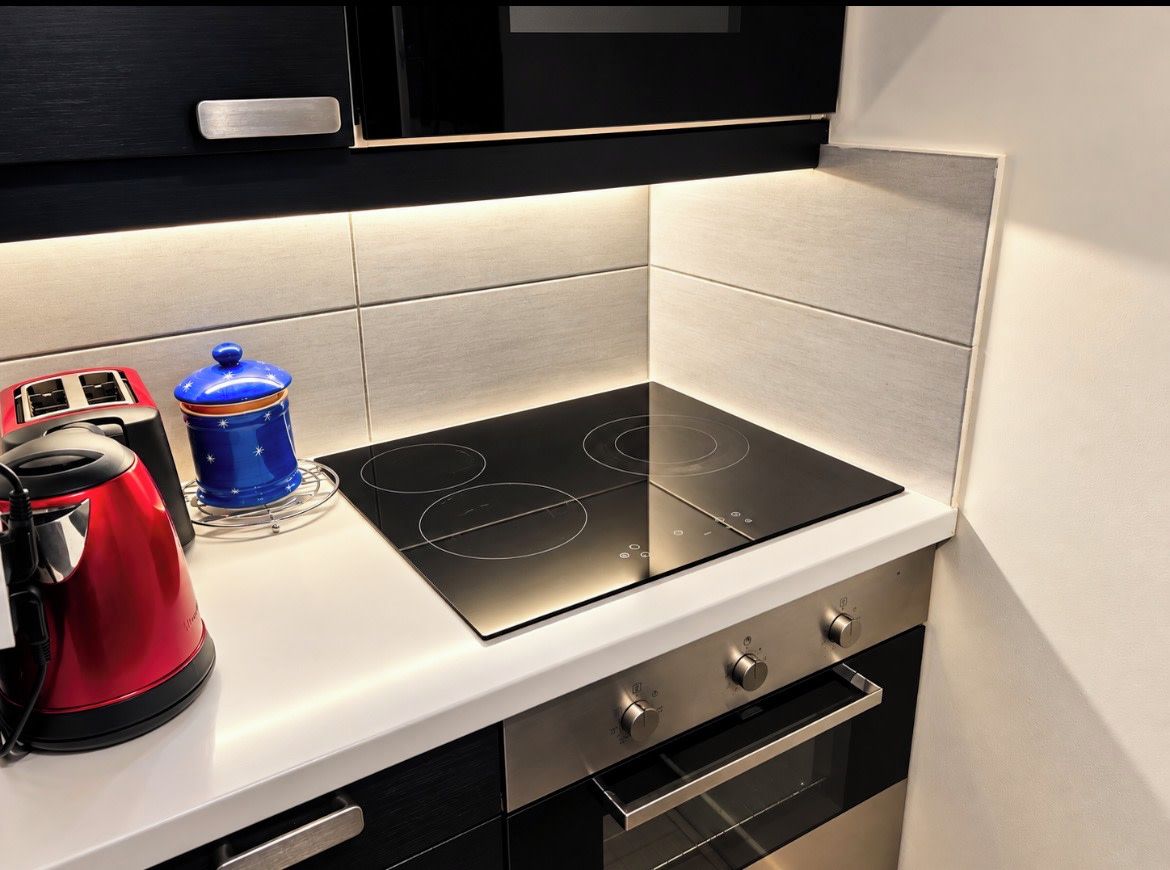Una cocina con un fogón de inducción negro, un hervidor rojo y un recipiente azul sobre la encimera.