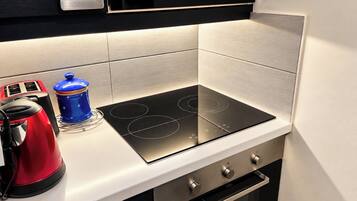 Una cocina con un fogón de inducción negro, un hervidor rojo y un recipiente azul sobre la encimera.