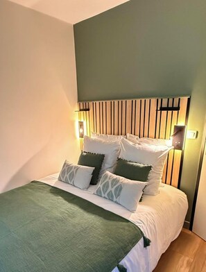 Una cama con cabecera de madera, varios almohadones y lámparas de noche.