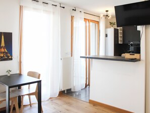 A modern kitchen with a flat-screen TV, wooden flooring, and a dining area with a table and chairs. - Cosy studio with balcony right next to Paris (Ivry-sur-Seine)