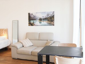 A modern living room with a sofa, a dining table, and a large landscape painting on the wall. - Cosy studio with balcony right next to Paris (Ivry-sur-Seine)