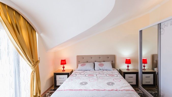 Una habitación de hotel con una cama, dos mesitas de noche, un espejo y una ventana con cortinas.
