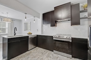 A modern kitchen with dark cabinetry, a stainless steel stove, and a dishwasher. - 3 Bedroom, 2 Full Bath Luxurious Park Circle Retreat (North Charleston)