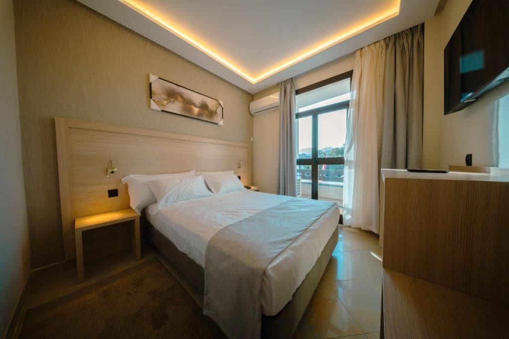 Une chambre d’hôtel avec un grand lit, des tables de chevet, un bureau et une fenêtre avec des rideaux.