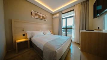 Une chambre d’hôtel avec un grand lit, des tables de chevet, un bureau et une fenêtre avec des rideaux.