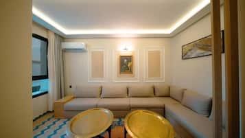 Una sala de estar con un sofá, dos mesitas, un cuadro y una ventana con cortinas.