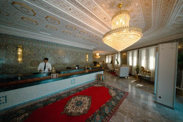 A reception area with a patterned wall, a red carpet, and a chandelier.