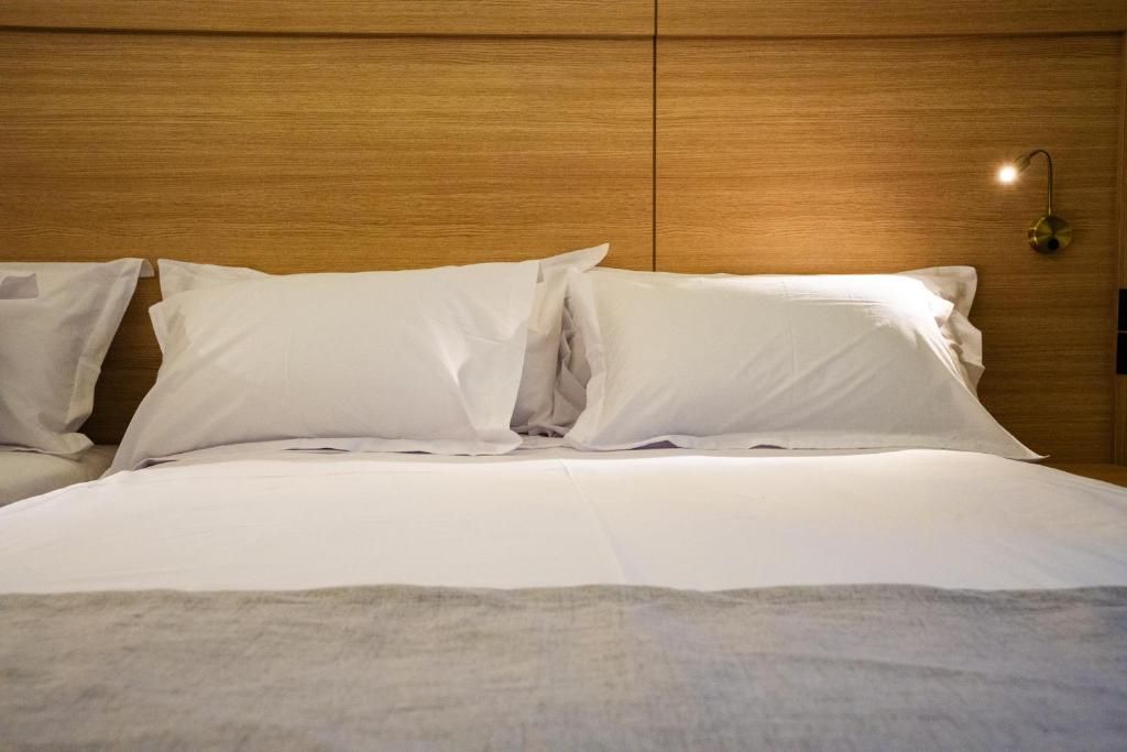 A neatly made bed with white linens and pillows, a wooden headboard, and a wall-mounted light fixture.