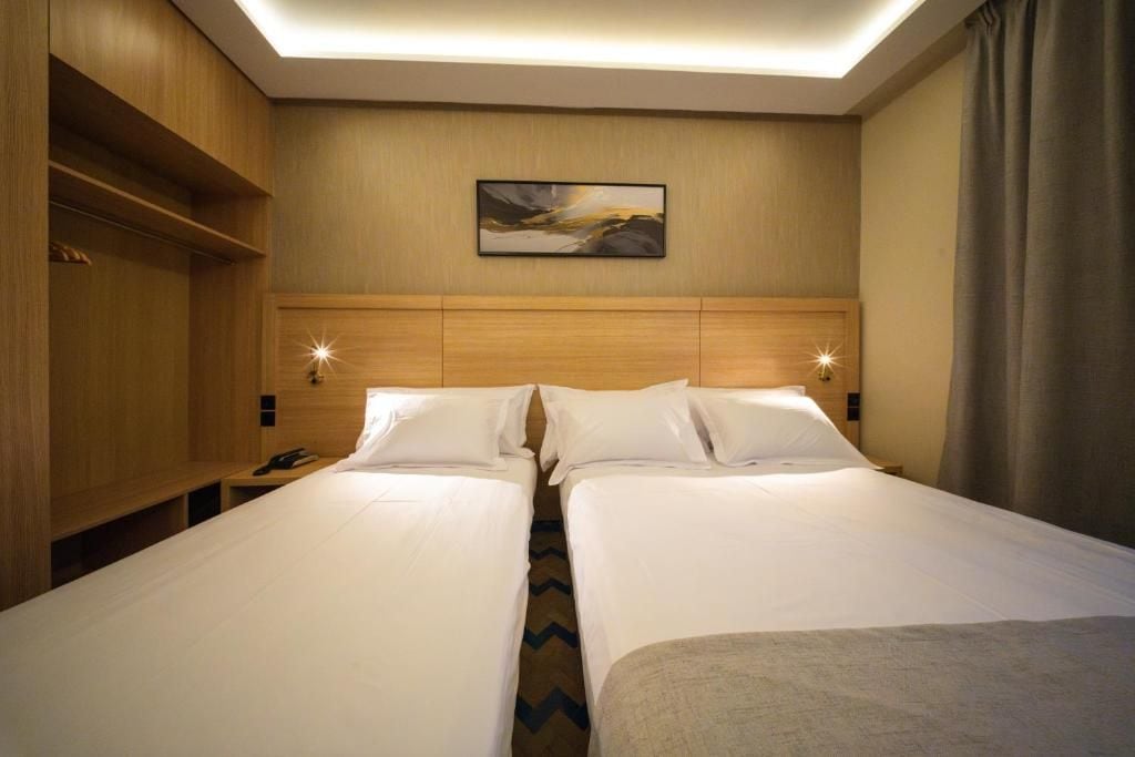 Ein Hotelzimmer mit zwei Betten, einem Holzkopfteil, einem Bild an der Wand und einem Nachttisch mit Telefon.