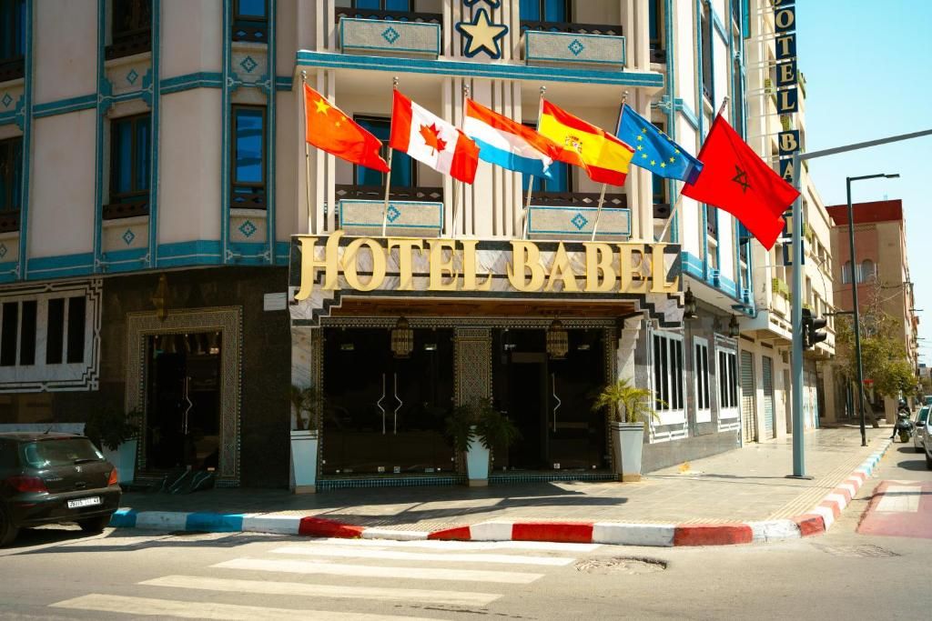 A hotel with a prominent sign, multiple flags, and a street view.
