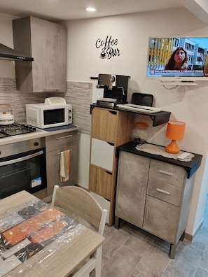 A compact kitchen with a coffee bar sign, a microwave, a stove, and a television displaying a news program. - Charming, cozy apartment on the mezzanine level, with a kitchen, bedroom, bathroom, and hallway (Alcamo)