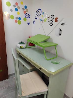 A room with a green desk, a small stool, a white cabinet, and a wall with colorful circular decorations. - Charming, cozy apartment on the mezzanine level, with a kitchen, bedroom, bathroom, and hallway (Alcamo)