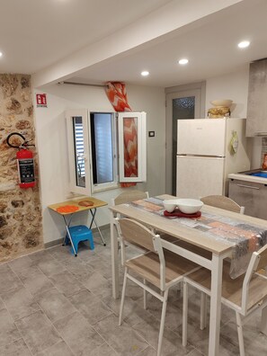 A compact kitchen with a dining area, a fire extinguisher, and a window with blinds. - Charming, cozy apartment on the mezzanine level, with a kitchen, bedroom, bathroom, and hallway (Alcamo)