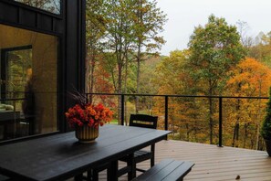 A wooden deck with a table and chairs, overlooking a forest with autumn foliage. - Hilltop Luxury Cabin Views, Sauna & Hot Tub (South Bloomingville)