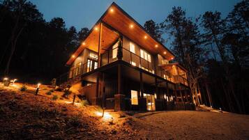 A two-story wooden cabin with a balcony, surrounded by trees.