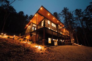 A two-story wooden cabin with a balcony, surrounded by trees.