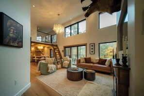 A spacious living area with a high ceiling, a staircase leading to an upper level, and a large window providing a view of the outdoors.