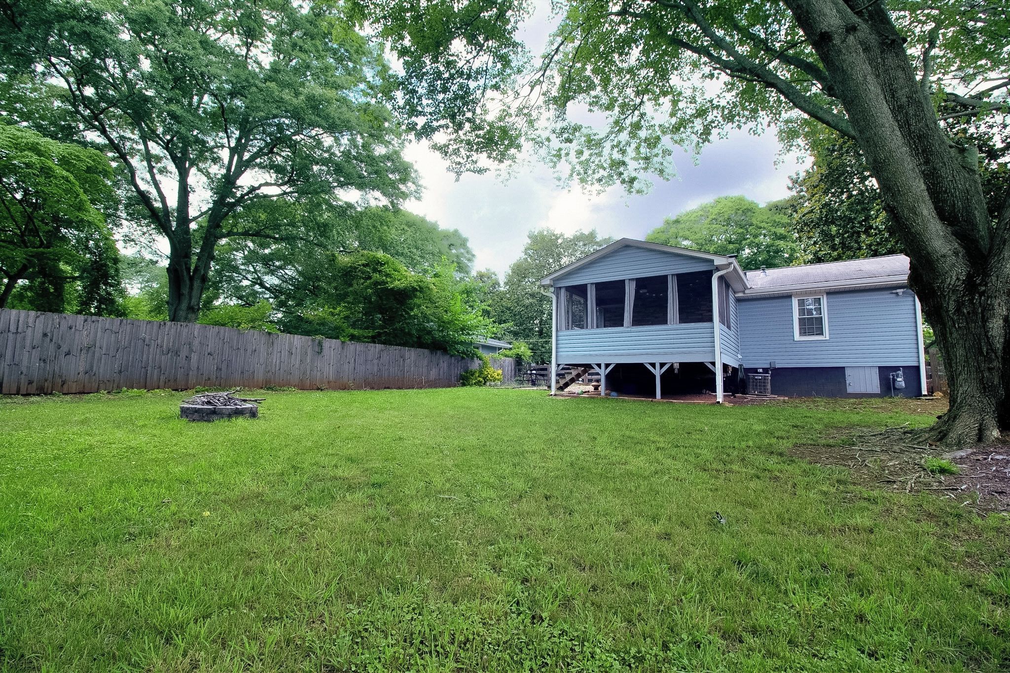 A residential property with a fenced backyard, a house with a porch, and a large tree.