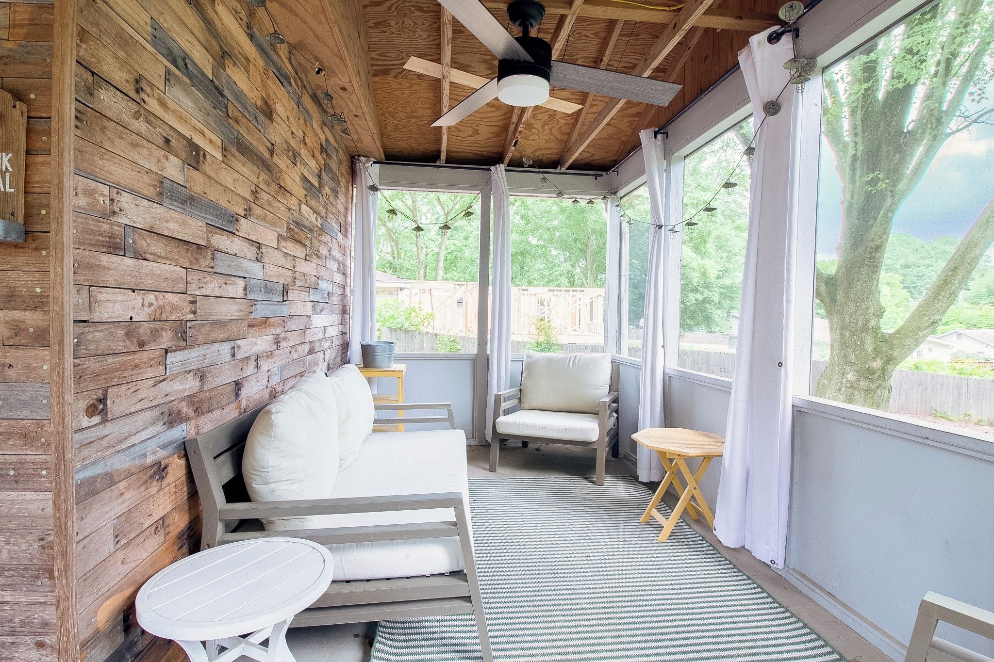 A covered outdoor seating area with a wooden wall, a ceiling fan, and a view of the outdoors.