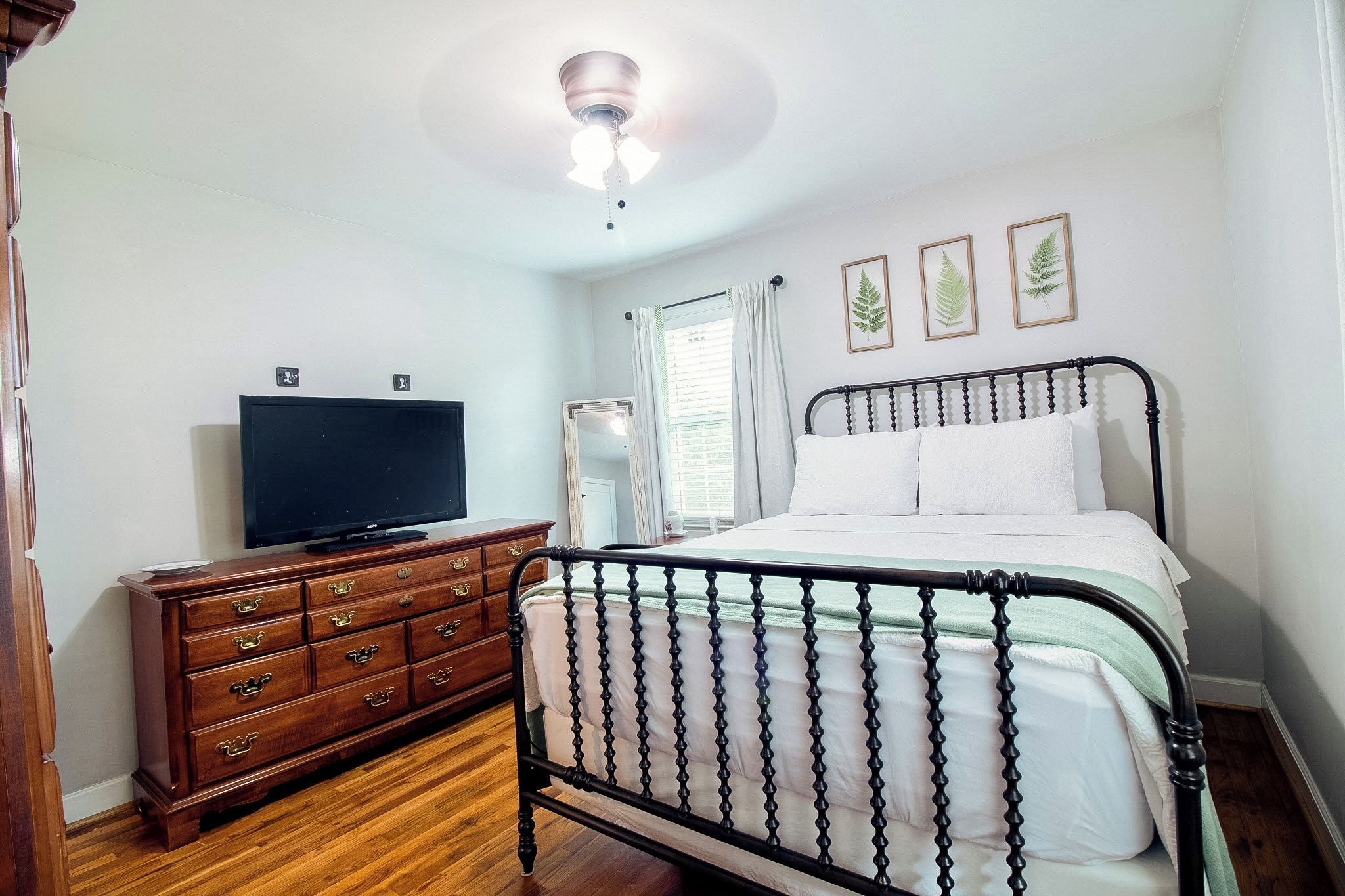 Un dormitorio con cama, cómoda, televisor y ventilador de techo.