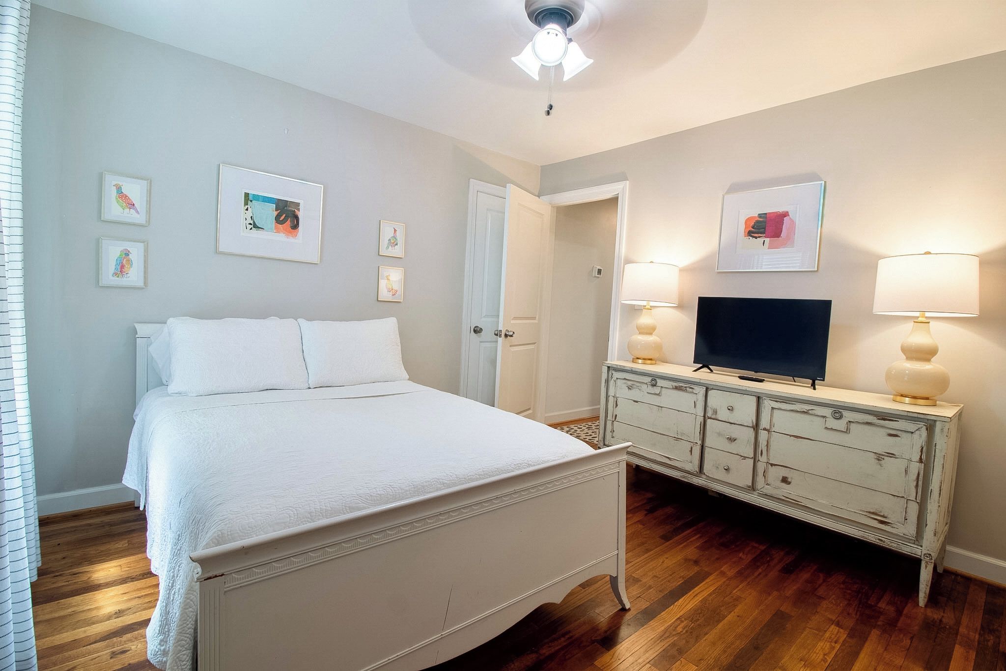 Une chambre à coucher avec un lit, une commode, un téléviseur et des œuvres d’art accrochées aux murs.