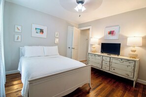 Une chambre à coucher avec un lit, une commode, un téléviseur et des œuvres d’art accrochées aux murs.