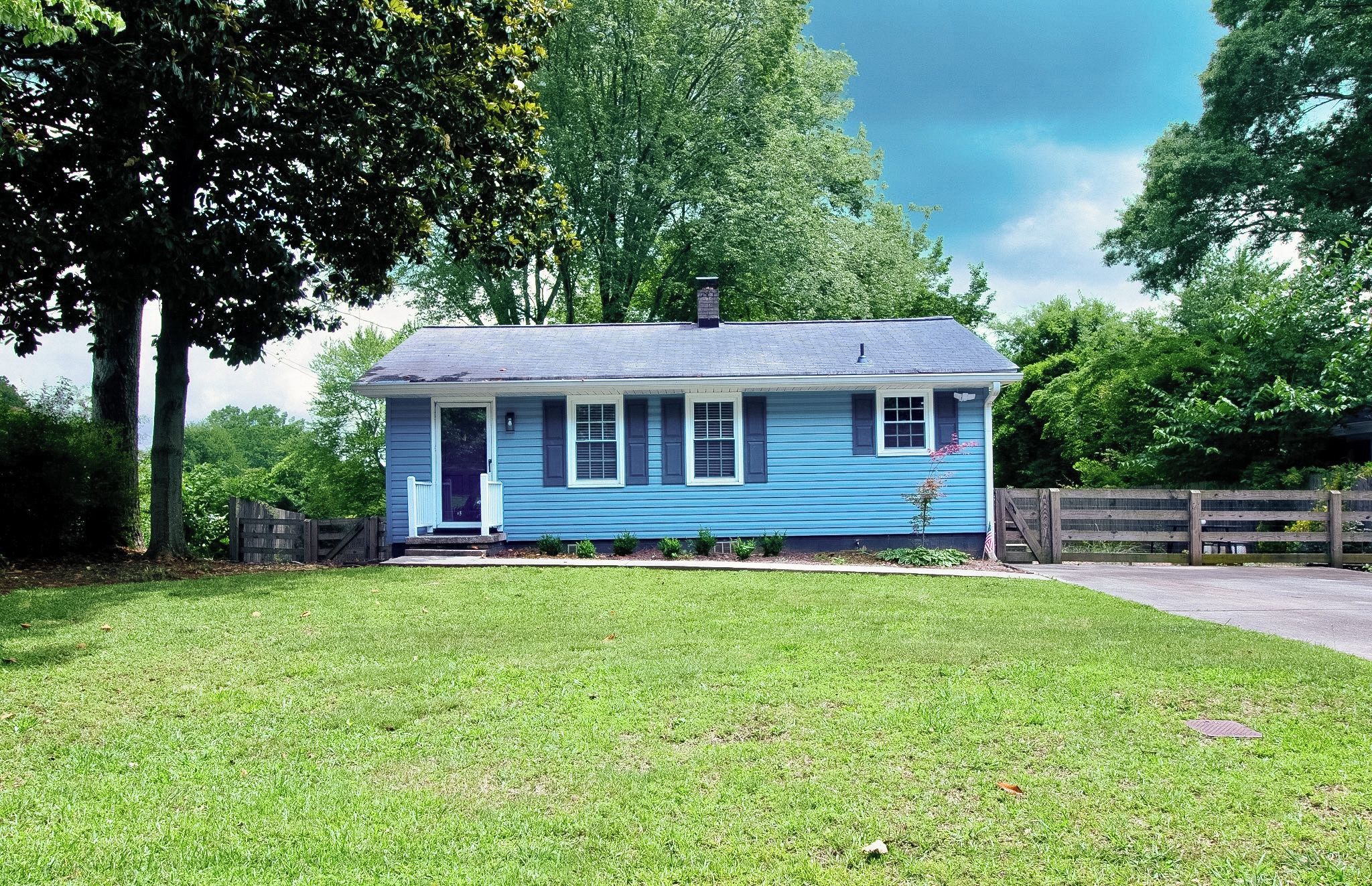A single-story house with a front porch, a small garden, and a wooden fence.