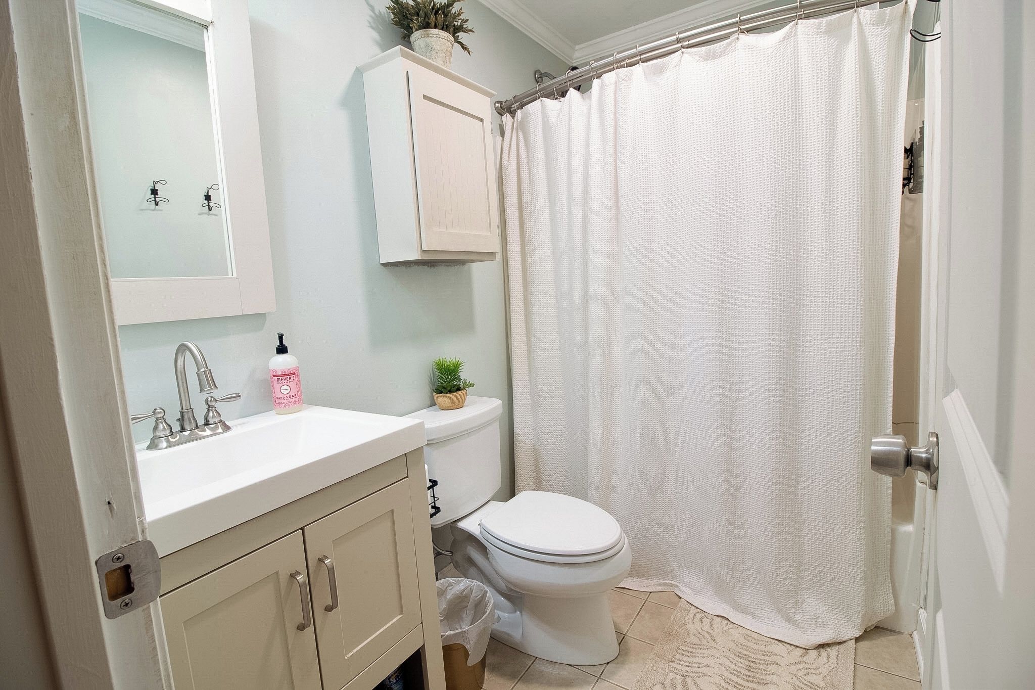 A bathroom with a white sink, a toilet, a shower curtain, and a cabinet.