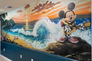 A mural of Mickey Mouse playing guitar on a wave with a sunset in the background. - Pool Table, Air Hockey, Swing, Basketball, Themed Rooms: Coastal Cove Retreat (Clermont)
