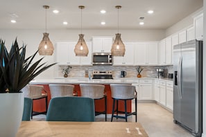 A modern kitchen with white cabinets, a stainless steel refrigerator, and a central island with bar stools. - Pool Table, Air Hockey, Swing, Basketball, Themed Rooms: Coastal Cove Retreat (Clermont)