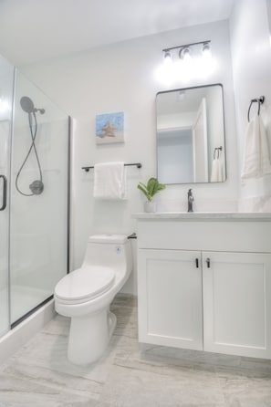 Ein modernes Badezimmer mit einer Duschkabine, einer Toilette, einem Waschbecken mit Spiegel und einem Handtuchhalter.