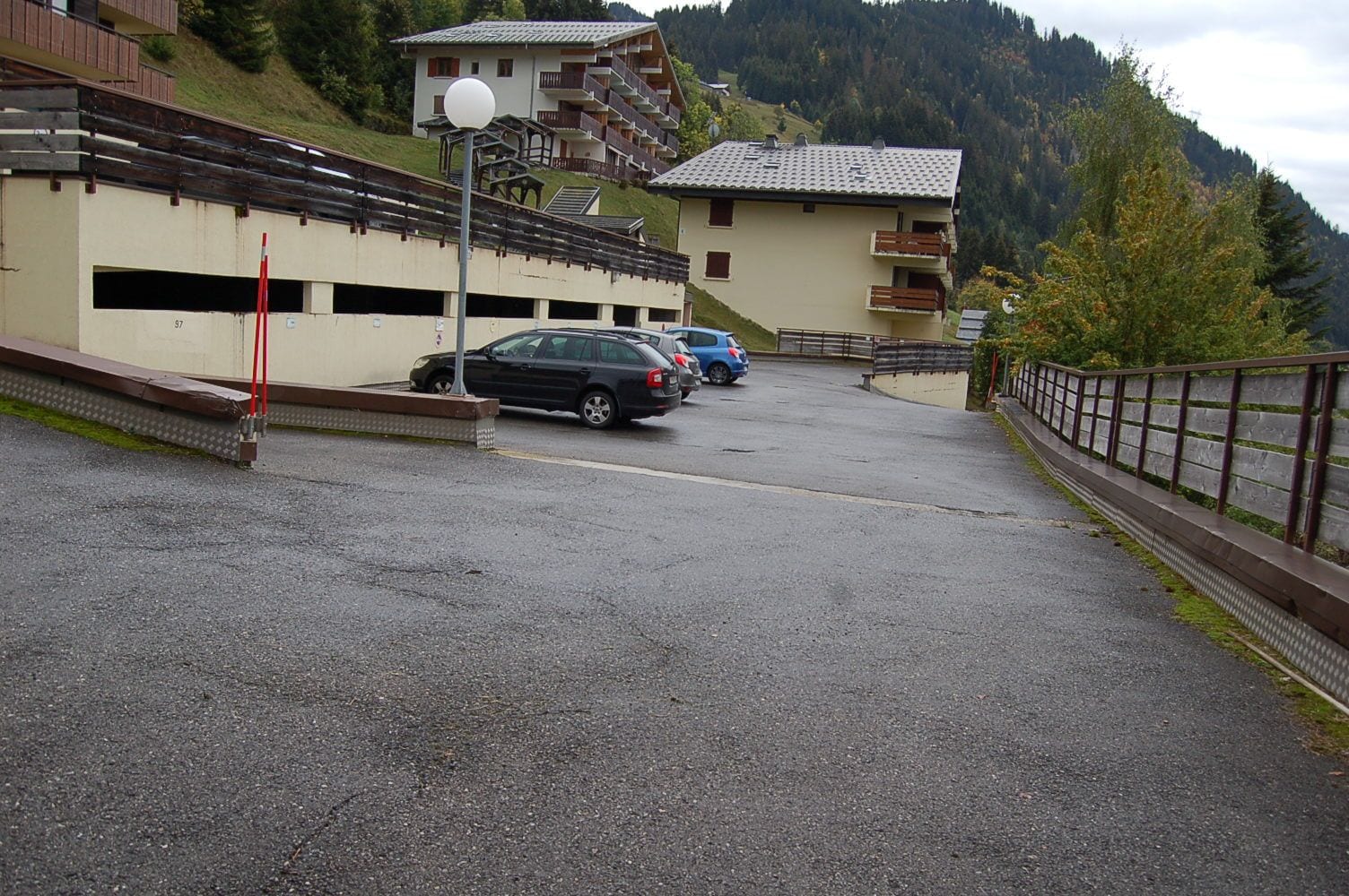Ein Parkplatz mit Autos, ein Gebäude mit Balkonen und eine Bergkulisse im Hintergrund.