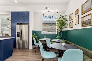 A modern kitchen with a built-in fridge, a dining area with round tables and chairs, and a green accent wall. - TWO full houses with a private pool, hot tub, gym, sauna, massage chair, cold plunge, movie projector, astroturf, axe throwing, corn hole and other lawn games! Unwind in this relaxing Paradise Oasis and let your worries drift away! (Austin)