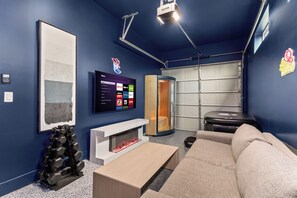 A modern living room with a flat-screen TV, a fireplace, a sofa, and a storage unit. - TWO full houses with a private pool, hot tub, gym, sauna, massage chair, cold plunge, movie projector, astroturf, axe throwing, corn hole and other lawn games! Unwind in this relaxing Paradise Oasis and let your worries drift away! (Austin)