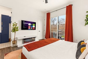 A modern bedroom with a bed, a flat-screen TV mounted on the wall, and a sliding glass door leading to an outdoor area. - TWO full houses with a private pool, hot tub, gym, sauna, massage chair, cold plunge, movie projector, astroturf, axe throwing, corn hole and other lawn games! Unwind in this relaxing Paradise Oasis and let your worries drift away! (Austin)