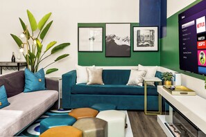 A modern living room with a teal sofa, a coffee table, and a green accent wall. - TWO full houses with a private pool, hot tub, gym, sauna, massage chair, cold plunge, movie projector, astroturf, axe throwing, corn hole and other lawn games! Unwind in this relaxing Paradise Oasis and let your worries drift away! (Austin)